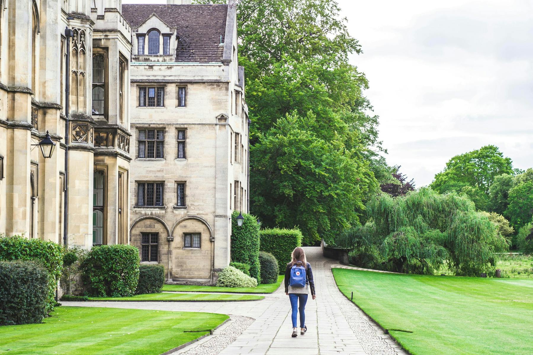 A woman walking along a road beside a building at King's College, Cambridge, UK.