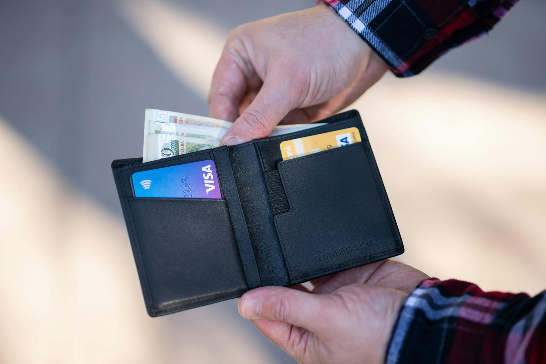 A black leather bifold wallet in a person's hands.