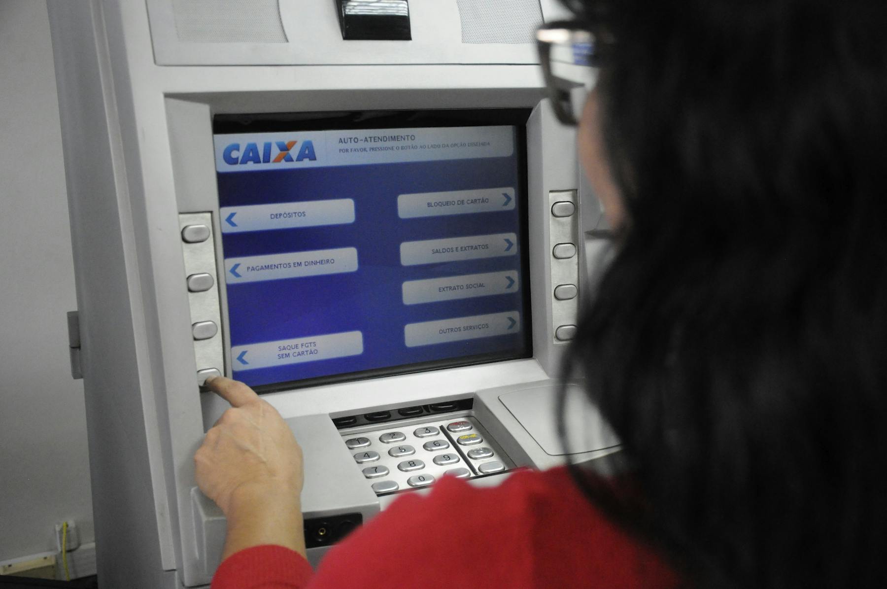 Mulher realiza saque sem cartão no caixa eletrônico da Caixa Econômica Federal