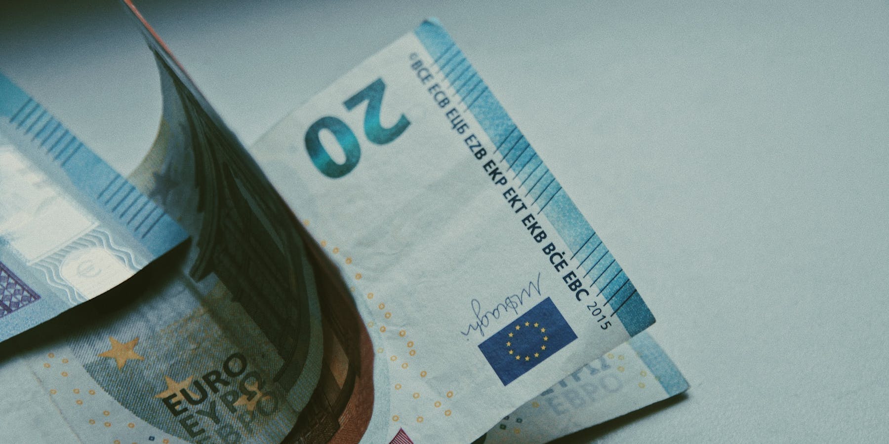 A closeup of four 20-euro banknotes on a white surface.