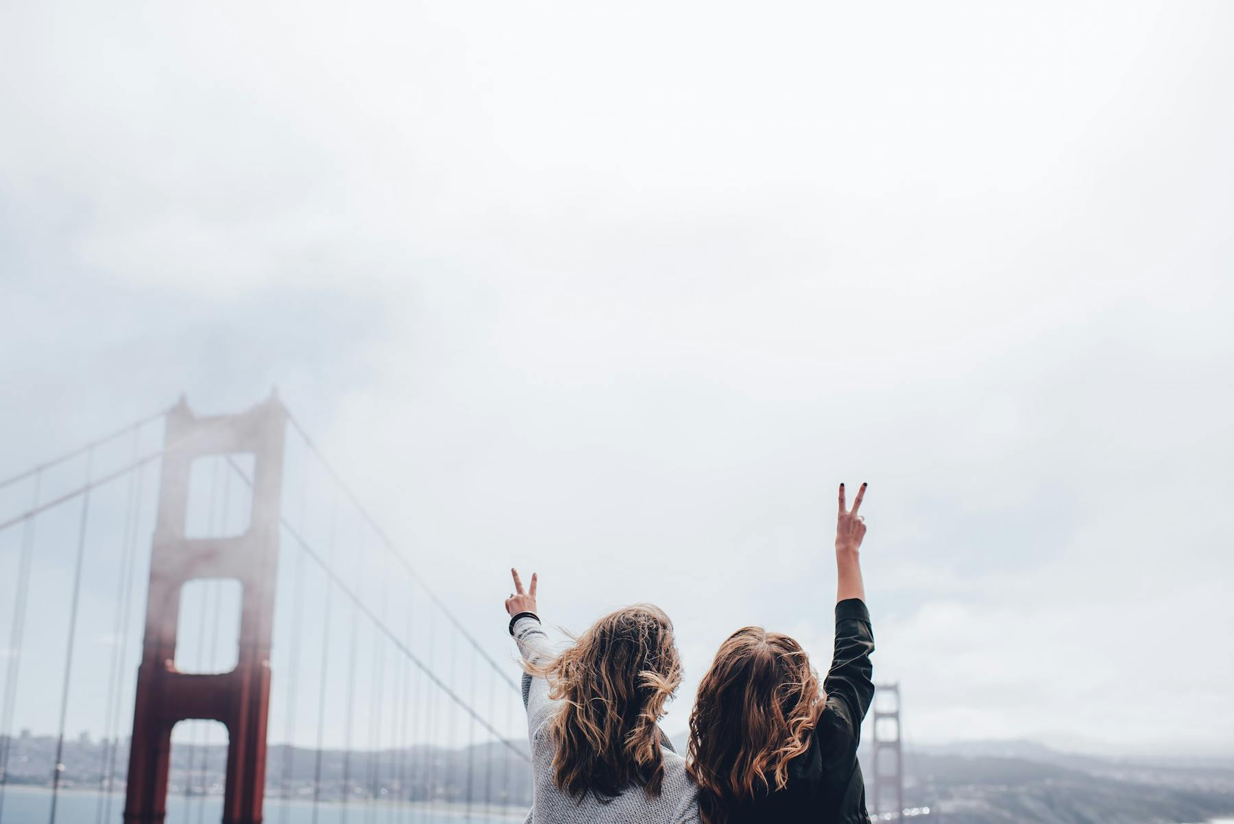 Two women making the peace sign by the Golden Gate Bridge, San Francisco, United States.